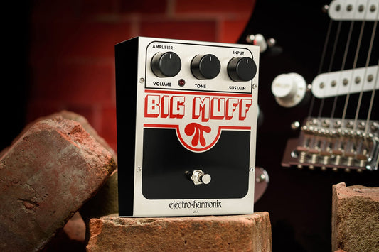  ELECTRO-HARMONIX EHX U.S. BIG MUFF PI PROMO PHOTO FRONT AND LEFT SIDE VIEW ON RED BRICKS WITH BLACK GUITAR AND RED BRICK BACKGROUND